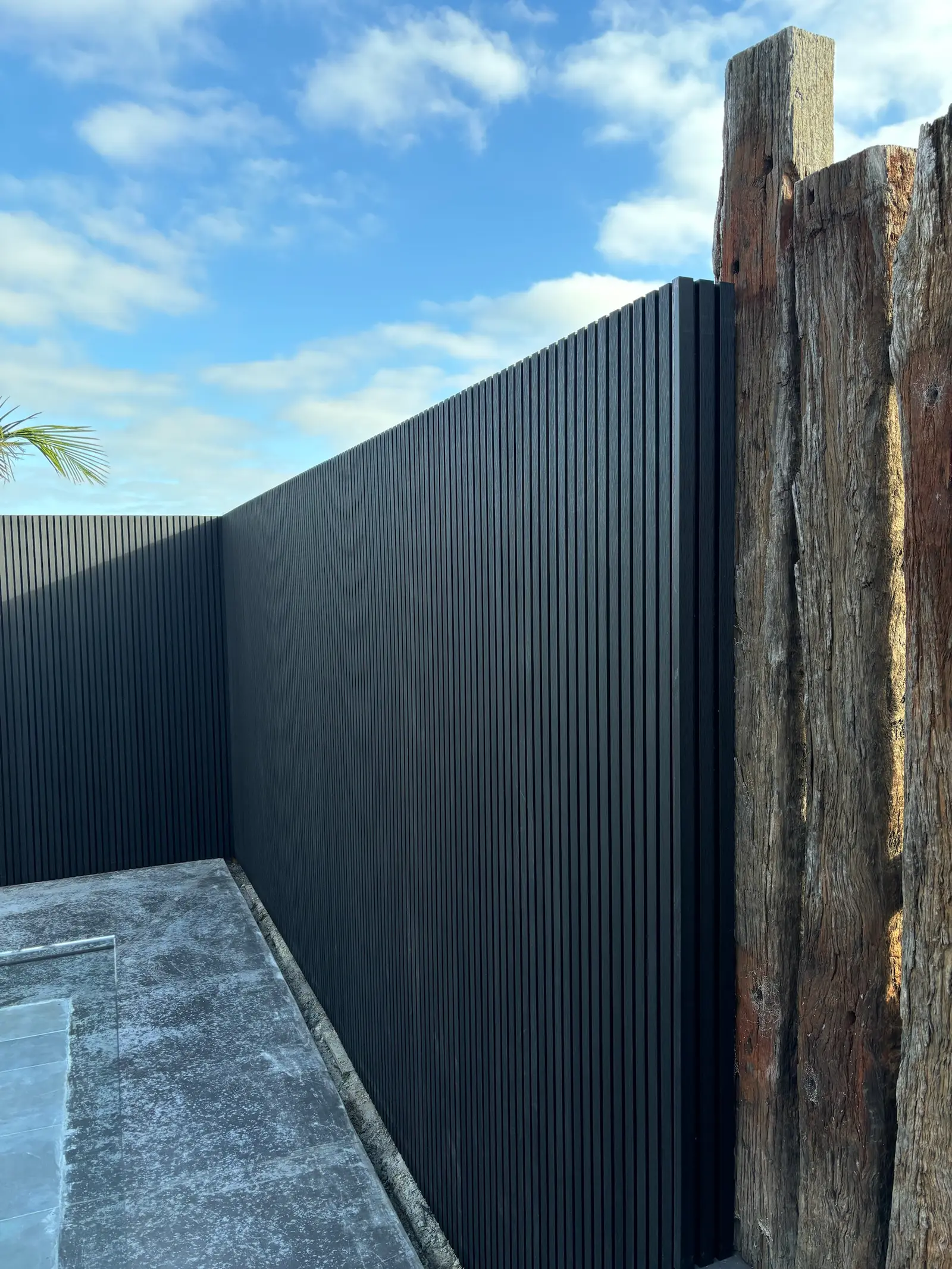Close view of the black slat fence finishing against weathered reclaimed timber sleeper posts