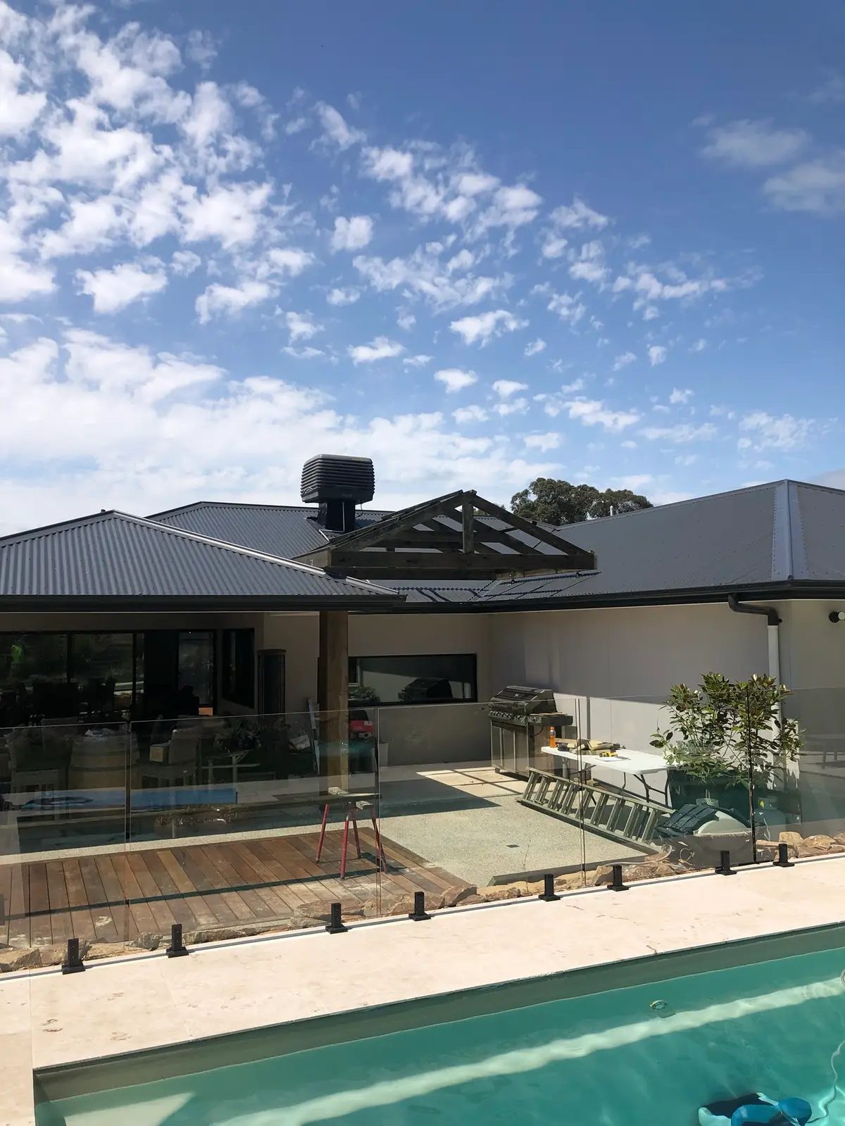Exposed timber gable truss above a covered alfresco on a rendered home, seen across a pool and glass fence during construction