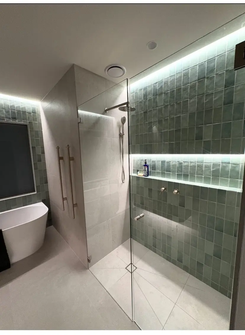 Renovated bathroom with a frameless walk-in shower, sage-green tiled walls lit by concealed LED strips, brass fittings and a freestanding bath