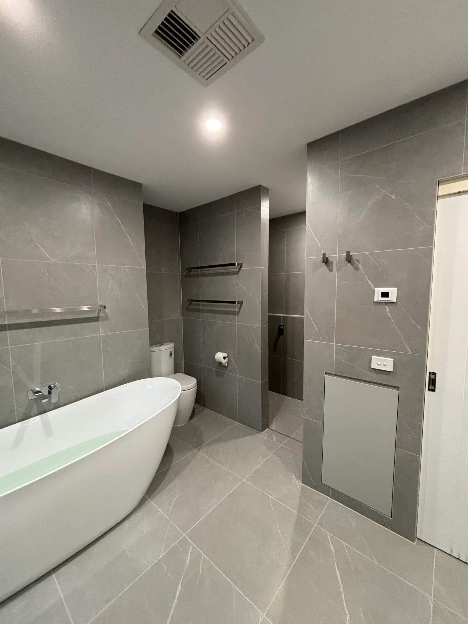 The same bathroom from the other end: freestanding bath, wall-mounted mixer, toilet, towel rails and a recessed storage panel in the tiled wall
