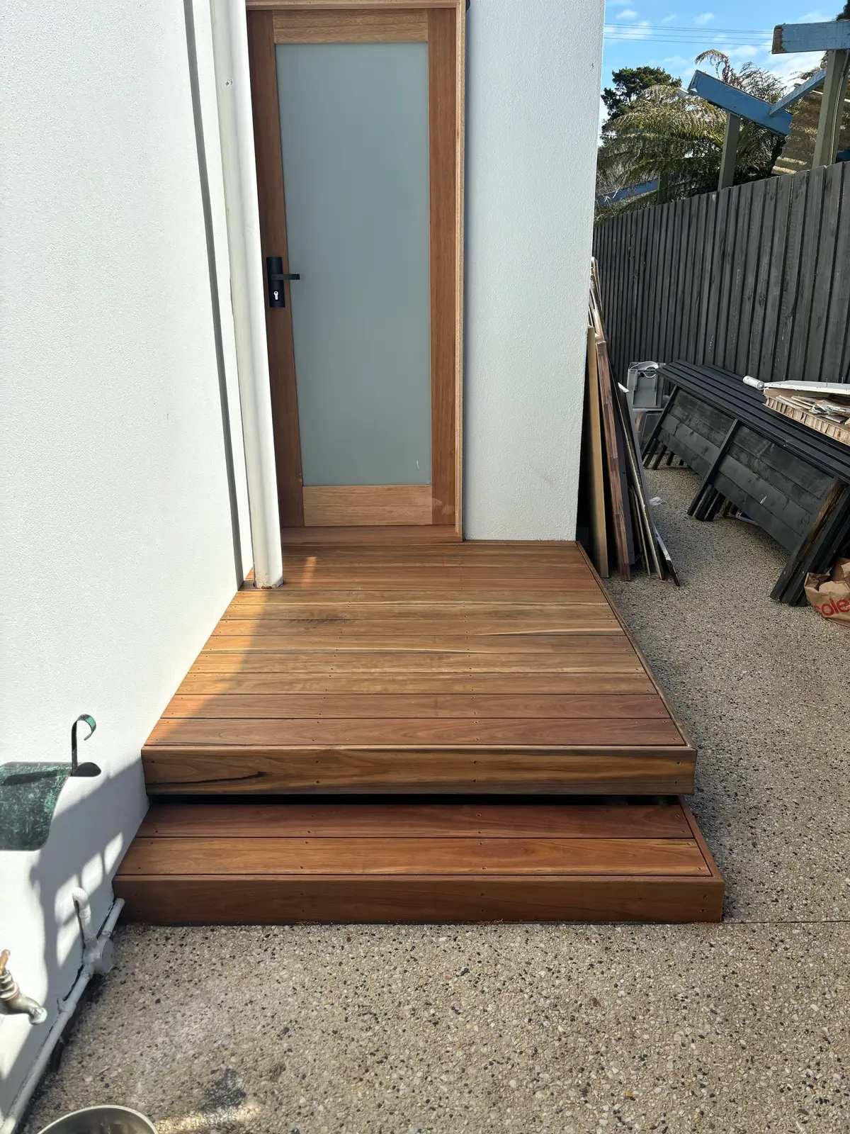 Two-level hardwood landing and step at a timber-framed side door on a rendered wall, beside a concrete path