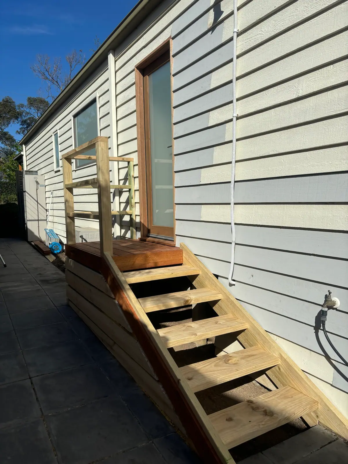 Hardwood landing at a rear door with open-tread timber stairs, handrail and horizontal board screening beside weatherboard cladding
