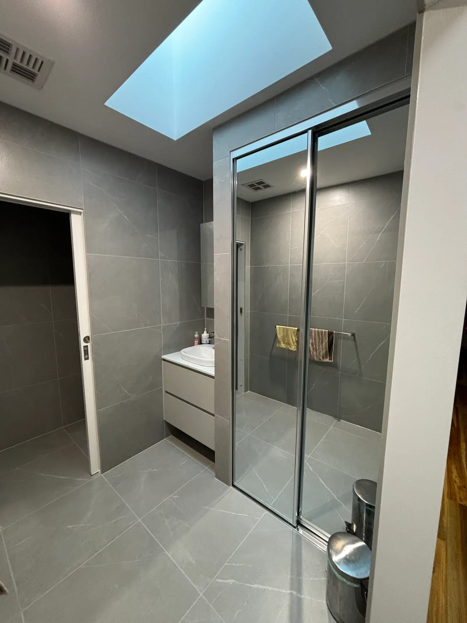 Grey-tiled ensuite with a skylight overhead, wall-hung vanity with single basin, and mirrored sliding doors